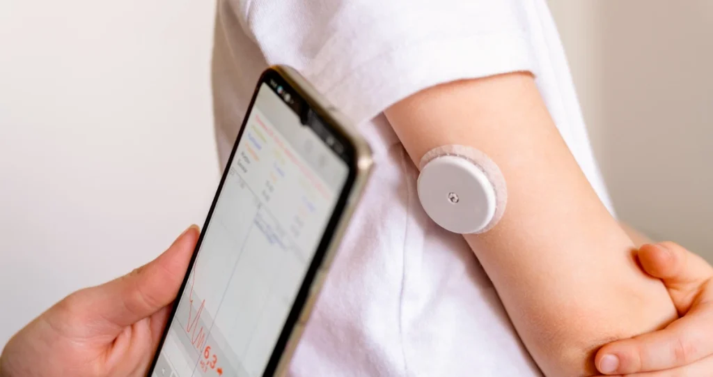 Person trägt Biosensor-Patch am Arm mit EKG-Daten auf dem Smartphone